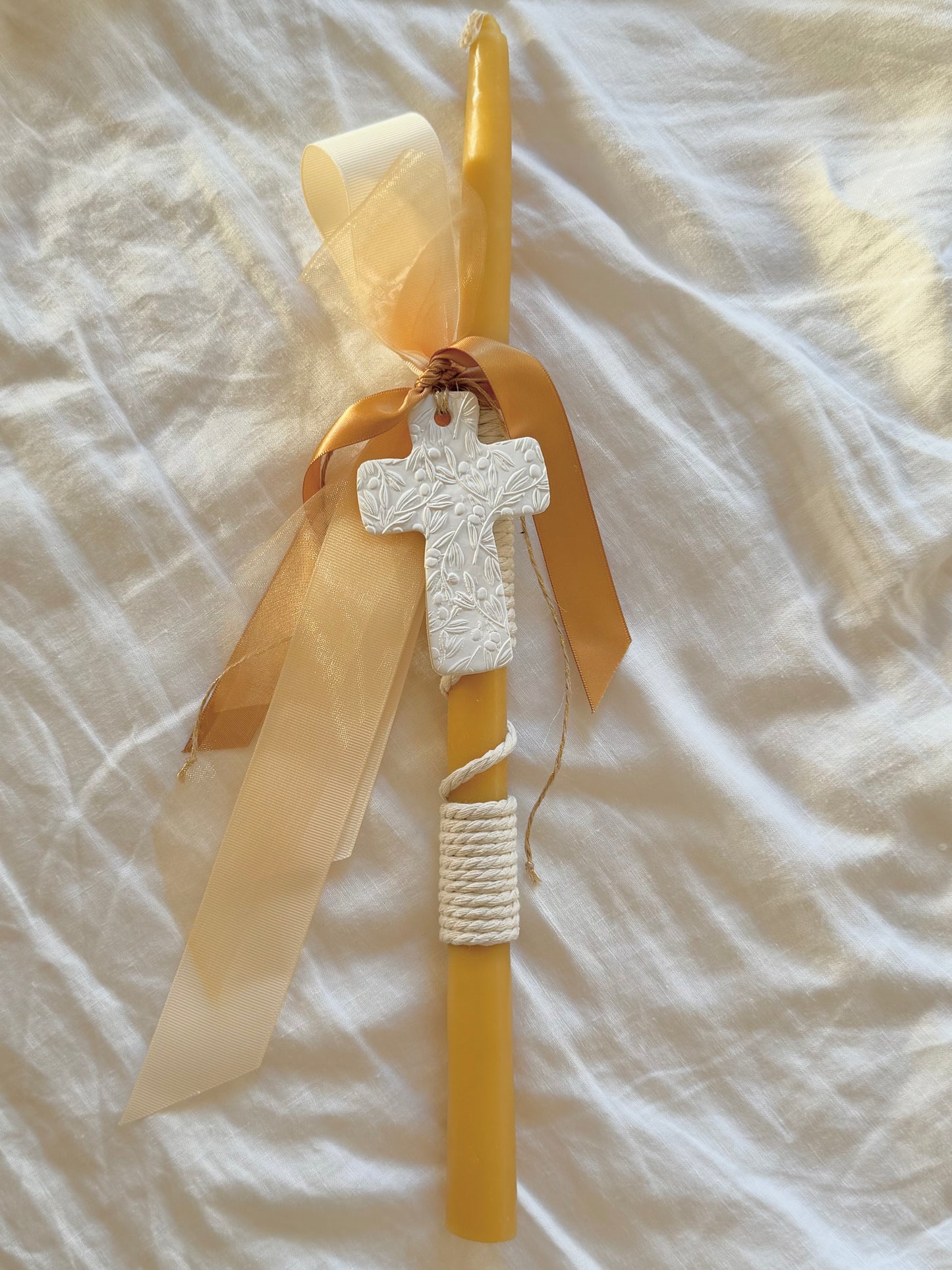 Yellow candle with a white cross and beige ribbon on a textured white surface