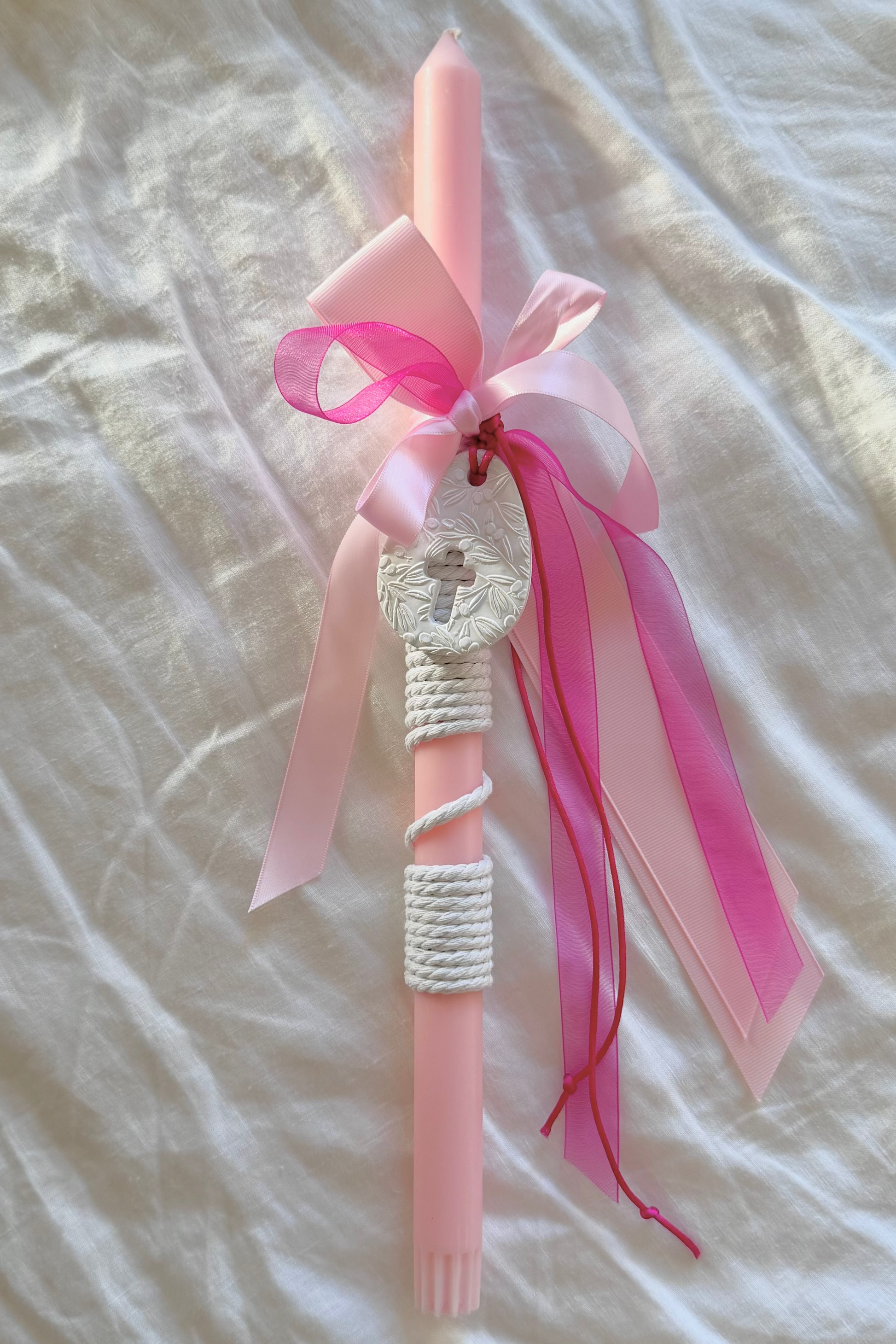Pink candle with ribbons on a textured white surface